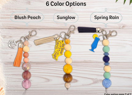 Three keychains with different color options labeled 'Blush Peach', 'Sunglow', and 'Spring Rain' on a wooden surface.
